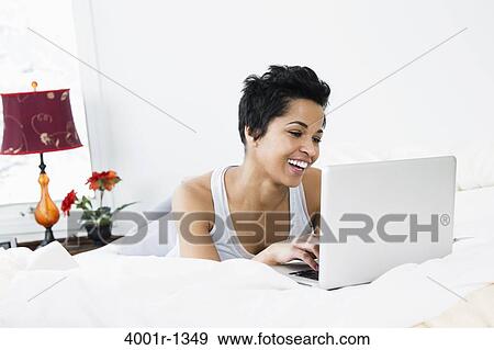 Mid adult woman using a laptop on the bed View Large Photo Image Stock Photo - Mid adult woman using a laptop on the bed. Fotosearch