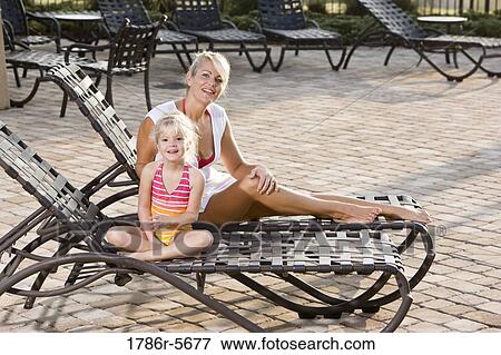 Stock Photo - Mother and daughter relaxing on pool lounge chairs. Fotosearch