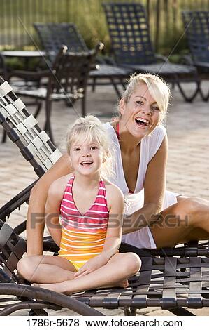 Stock Photo - Mother and daughter relaxing on pool lounge chairs. Fotosearch