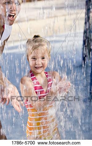 Stock Image - Mother and girl having fun under splashing water. Fotosearch