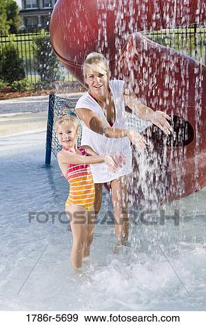Stock Photo - Mother and girl having fun under splashing water. Fotosearch
