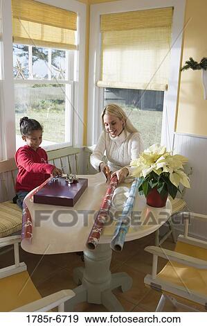 Mother and young daughter wrapping gifts on kitchen table by large windows View Large Photo Image Stock Photo - Mother and young daughter wrapping gifts on kitchen table by large windows. Fotosearch