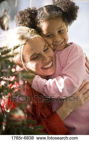 Mother with daughter in pajamas embracing next to Christmas tree View Large Photo Image Stock Photo - Mother with daughter in pajamas embracing next to Christmas tree. Fotosearch