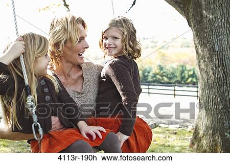 Stock Image - Mother with two daughters on swing. Fotosearch