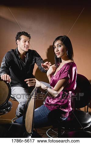 Stock Photo - Multiracial couple sitting on bar stools chatting. Fotosearch
