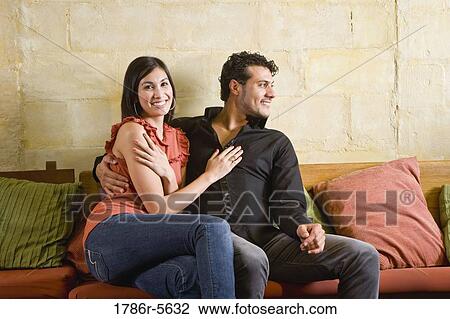 Multiracial couple sitting together on sofa View Large Photo Image Stock Image - Multiracial couple sitting together on sofa. Fotosearch
