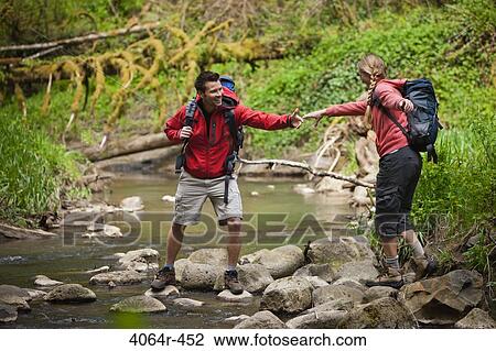 Stock Image - Portland, Oregon, USA, Man helping woman across creek. Fotosearch
