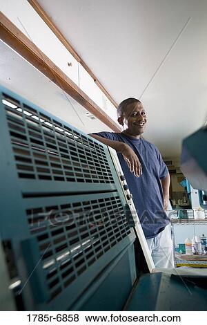Stock Photo - Portrait of a blue-collar man standing behind a printing machine. Fotosearch