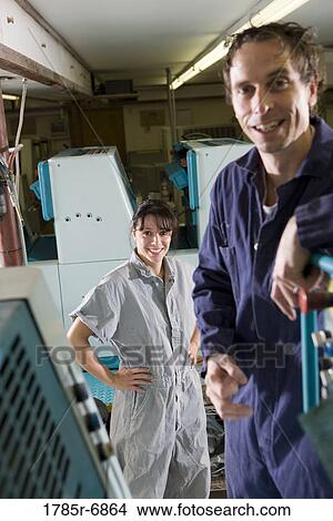 Portrait of a man and a woman in coveralls behind a printing machine View Large Photo Image Picture - Portrait of a man and a woman in coveralls behind a printing machine. Fotosearch