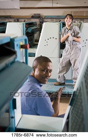 Picture - Portrait of a man and a woman in coveralls behind a printing machine. Fotosearch