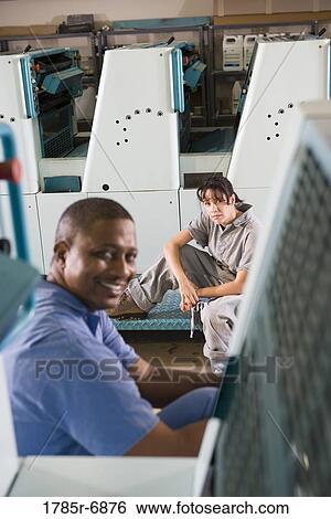 Stock Photograph - Portrait of a man and a woman in coveralls behind a printing machine. Fotosearch