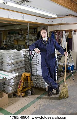 Portrait of a man in coveralls holding a broom in a warehouse View Large Photo Image Picture - Portrait of a man in coveralls holding a broom in a warehouse. Fotosearch