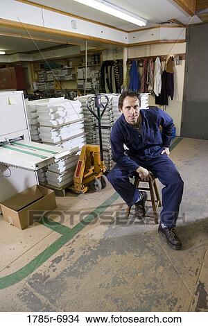 Portrait of a man sitting on a stool in a warehouse View Large Photo Image Picture - Portrait of a man sitting on a stool in a warehouse. Fotosearch