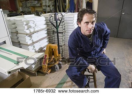 Stock Image - Portrait of a man sitting on a stool in a warehouse. Fotosearch