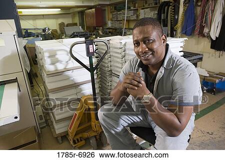 Stock Photograph - Portrait of a man sitting on a stool in a warehouse. Fotosearch
