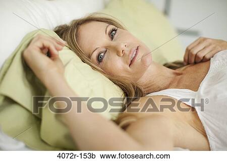 Stock Image - Portrait of a mature woman lying on the bed and smiling. Fotosearch