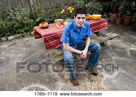 Stock Photo - Portrait of a smiling young man sitting in front of a picnic table. Fotosearch