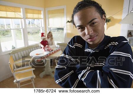 Portrait of a teenager boy with arms folded, family wrapping gifts in background View Large Photo Image Picture - Portrait of a teenager boy with arms folded, family wrapping gifts in background. Fotosearch