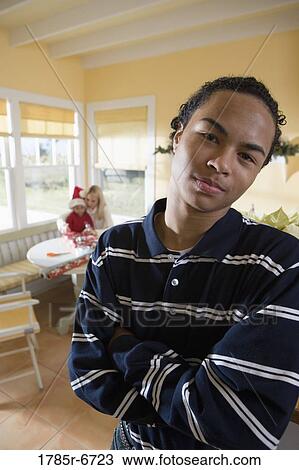 Portrait of a teenager boy with arms folded, family wrapping gifts in background View Large Photo Image Stock Image - Portrait of a teenager boy with arms folded, family wrapping gifts in background. Fotosearch