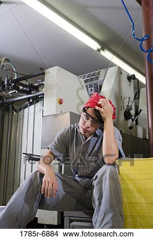 Portrait of a tired woman in coveralls sitting next to some machinery View Large Photo Image Picture - Portrait of a tired woman in coveralls sitting next to some machinery. Fotosearch