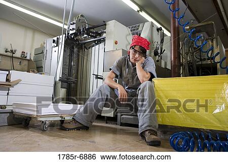 Portrait of a tired woman in coveralls sitting next to some machinery View Large Photo Image Stock Photograph - Portrait of a tired woman in coveralls sitting next to some machinery. Fotosearch