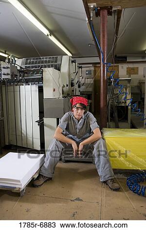 Stock Image - Portrait of a woman in coveralls sitting next to some machinery. Fotosearch