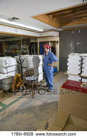 Stock Photo - Portrait of a woman standing next to a stool in a warehouse. Fotosearch