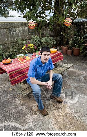Portrait of a young man sitting in front of a picnic table View Large Photo Image Stock Image - Portrait of a young man sitting in front of a picnic table. Fotosearch