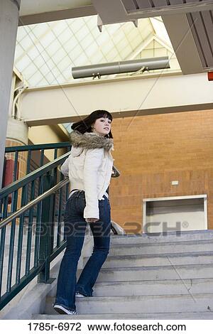 Stock Image - Portrait of a young woman climbing up a flight of stairs. Fotosearch
