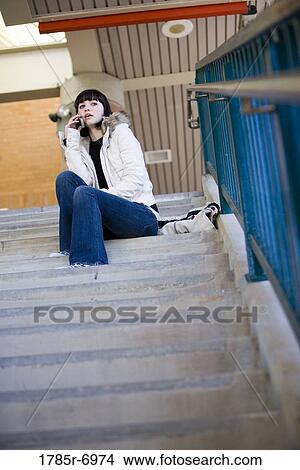 Portrait of a young woman sitting at the top of a concrete staircase on cellphone View Large Photo Image Picture - Portrait of a young woman sitting at the top of a concrete staircase on cellphone. Fotosearch