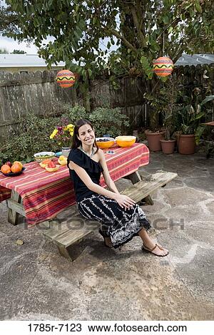 Stock Image - Portrait of a young woman sitting in front of a picnic table. Fotosearch