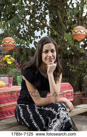 Stock Photography - Portrait of a young woman sitting in front of a picnic table. Fotosearch