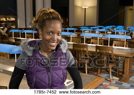 Stock Image - Portrait of a young woman standing in the reading room of a library. Fotosearch
