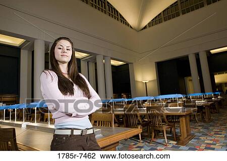 Stock Image - Portrait of a young woman standing in the reading room of a library. Fotosearch