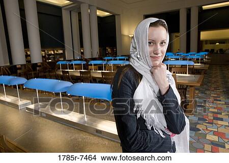 Portrait of a young woman wearing a head scarf standing in the reading room of a library View Large Photo Image Picture - Portrait of a young woman wearing a head scarf standing in the reading room of a library. Fotosearch