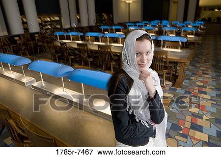 Portrait of a young woman wearing a head scarf standing in the reading room of a library View Large Photo Image Stock Photo - Portrait of a young woman wearing a head scarf standing in the reading room of a library. Fotosearch