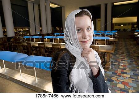 Stock Photograph - Portrait of a young woman wearing a head scarf standing in the reading room of a library. Fotosearch