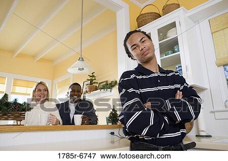 Portrait of an inter-racial teenage boy standing in kitchen with parents in the background View Large Photo Image Stock Photo - Portrait of an inter-racial teenage boy standing in kitchen with parents in the background. Fotosearch