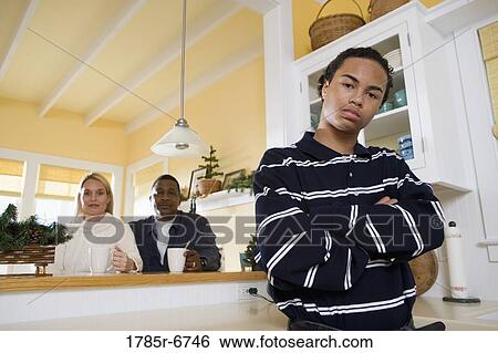 Portrait of an inter-racial teenage boy standing in kitchen with parents in the background View Large Photo Image Stock Photograph - Portrait of an inter-racial teenage boy standing in kitchen with parents in the background. Fotosearch