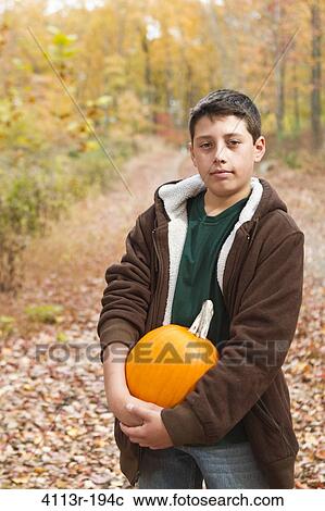 Stock Image - Portrait of boy carrying pumpkin in forest. Fotosearch