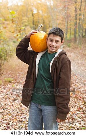 Stock Image - Portrait of boy carrying pumpkin in forest. Fotosearch