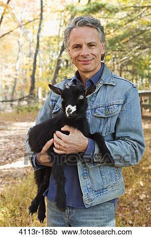 Stock Image - Portrait of farmer holding black lamb. Fotosearch