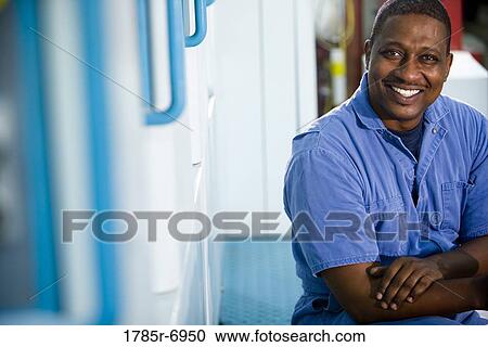 Stock Image - Portrait of man in coveralls next to some machinery. Fotosearch