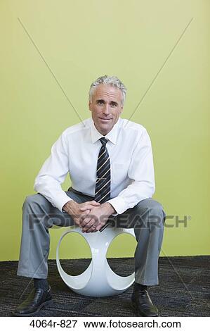 Portrait of mature businessman sitting on designer chair against yellow background View Large Photo Image Stock Photo - Portrait of mature businessman sitting on designer chair against yellow background. Fotosearch
