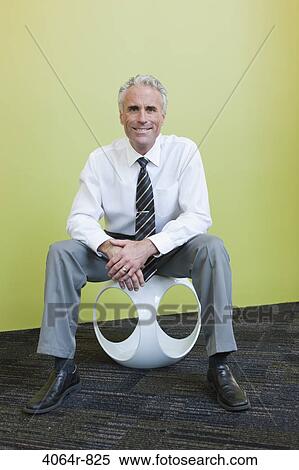 Portrait of mature businessman sitting on designer chair against yellow background View Large Photo Image Stock Photography - Portrait of mature businessman sitting on designer chair against yellow background. Fotosearch