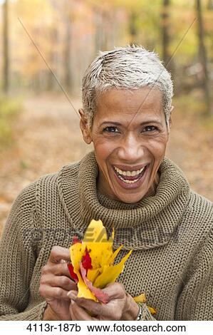 Stock Image - Portrait of mature woman holding Autumn leaves and laughing. Fotosearch