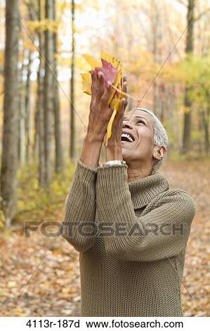 Stock Image - Portrait of mature woman holding Autumn leaves and laughing. Fotosearch