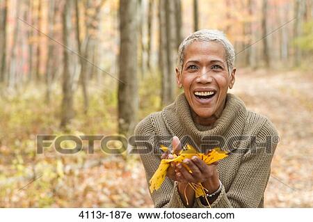 Stock Image - Portrait of mature woman holding Autumn leaves and laughing. Fotosearch