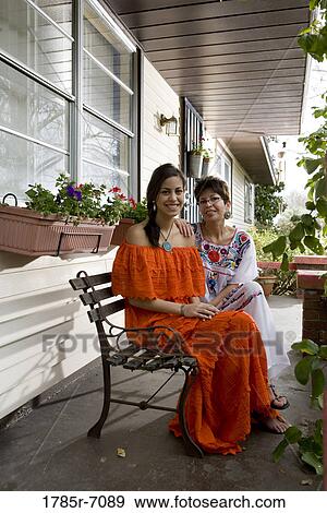 Stock Photo - Portrait of Mexican mother and daughter sitting on a bench on front porch. Fotosearch