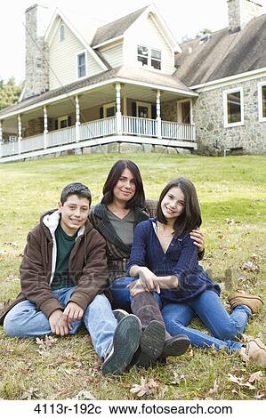 Stock Image - Portrait of smiling mother with two children sitting in front of large house. Fotosearch